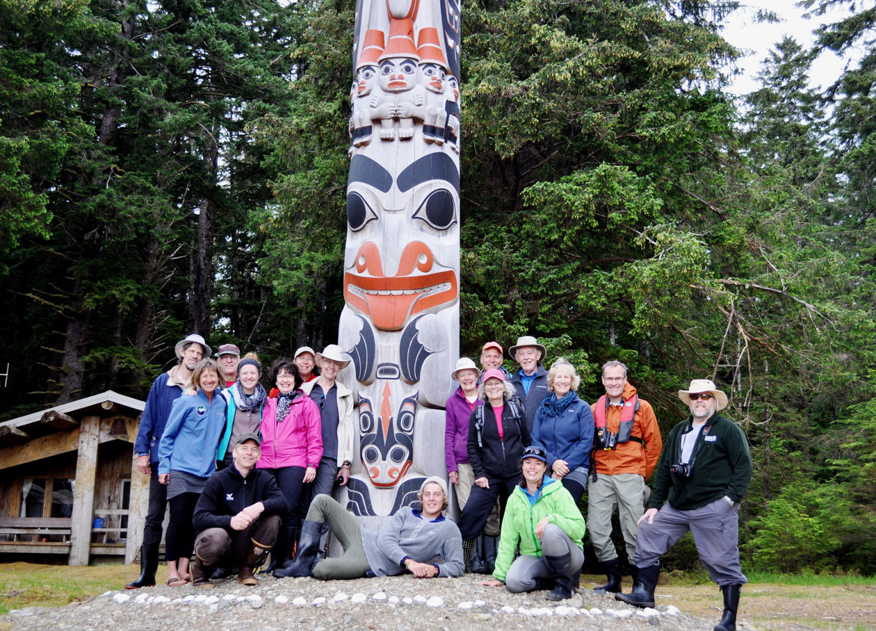 A happy Bluewater Adventures group of guests pose in front of a totem pole at Windy Bay