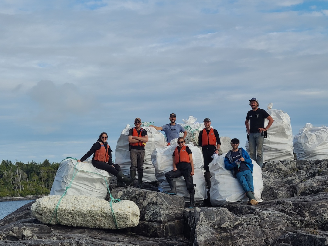 Bluewater Adventures crew members stand by several large white lift bags full of derelict fishing gear and other marine debris cleaned off of the central BC coast.